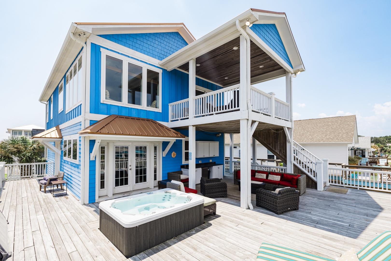 Charming blue beach house with covered deck, hot tub, and outdoor seating where you can unwind after sunny coastal adventures.