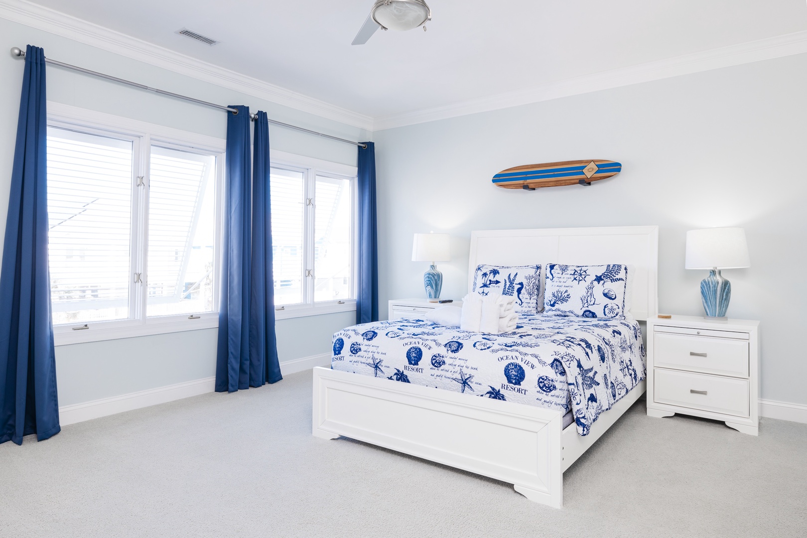 Drift off in your coastal-themed bedroom featuring crisp white furnishings, nautical blue accents, and a charming surfboard wall art that whispers of ocean adventures.