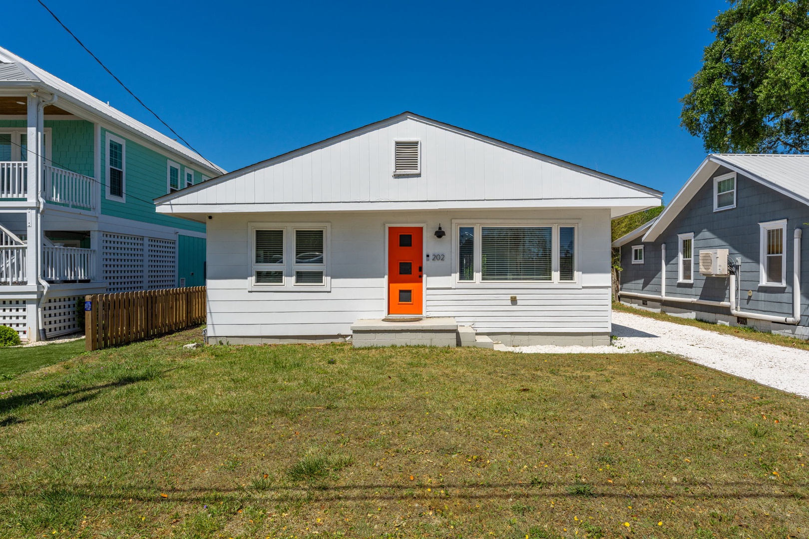 Charming white cottage with vibrant orange door sits in quiet residential neighborhood, featuring modern updates and easy parking access.