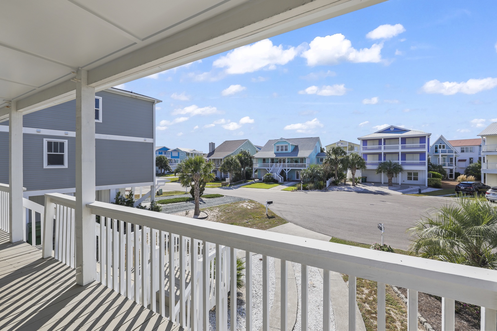 Covered porch overlooking the tranquil coastal neighborhood, lined with palm trees and colorful beach homes under sunny skies.