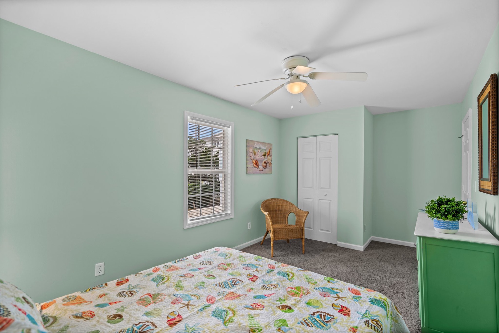 Relax in your peaceful bedroom with soothing mint walls, cheerful bedding, and a cozy wicker chair perfect for unwinding.