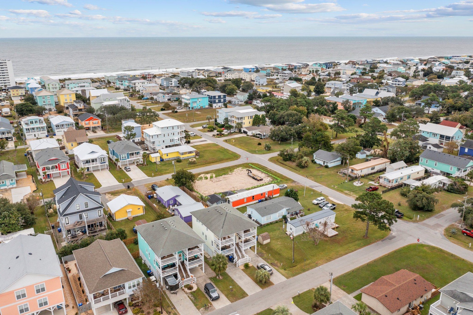 Aerial view of a charming coastal community with colorful beach houses nestled between tree-lined streets and the ocean shoreline.