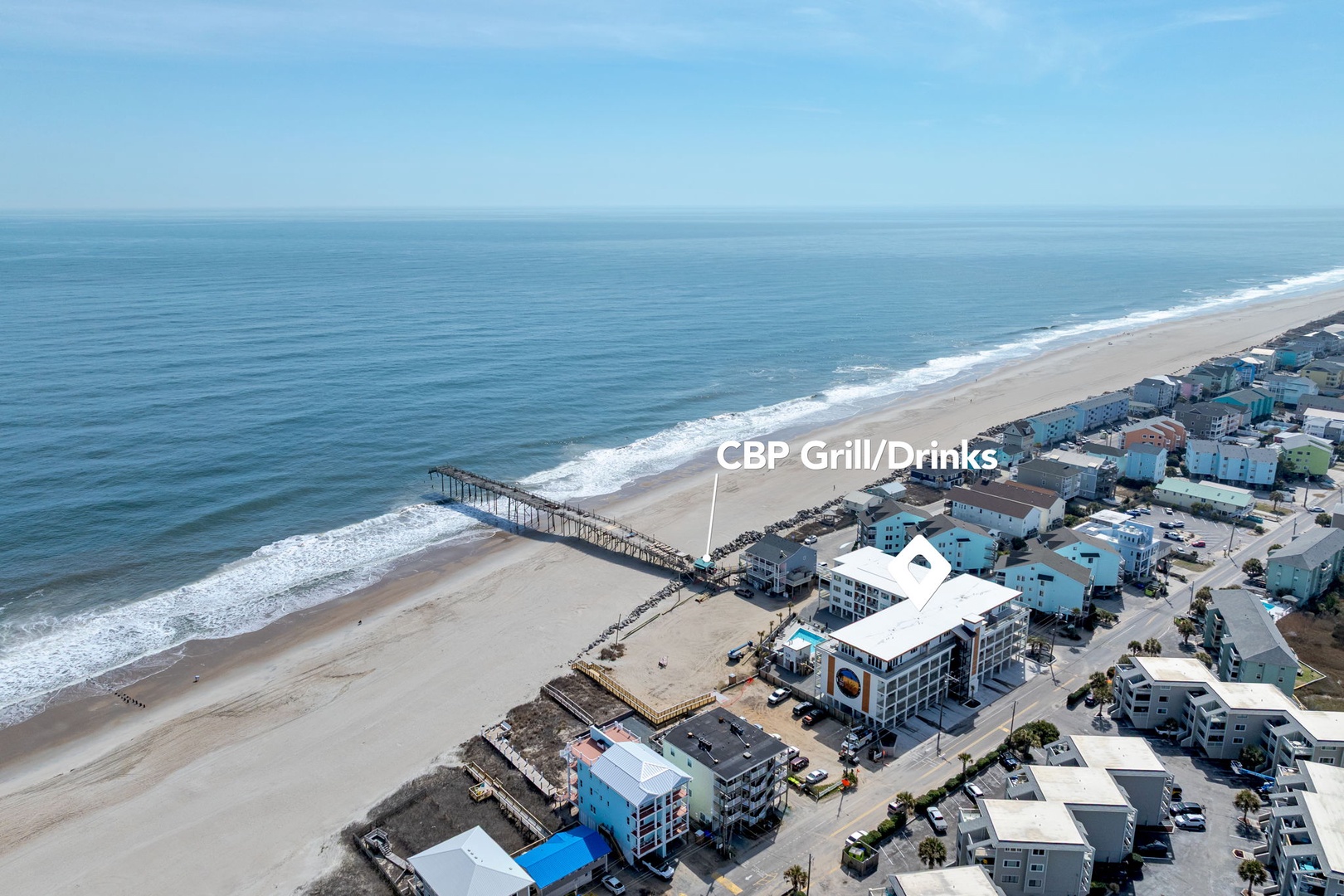 Aerial view of pristine coastline with sandy beach, fishing pier, and colorful beachfront community buildings.