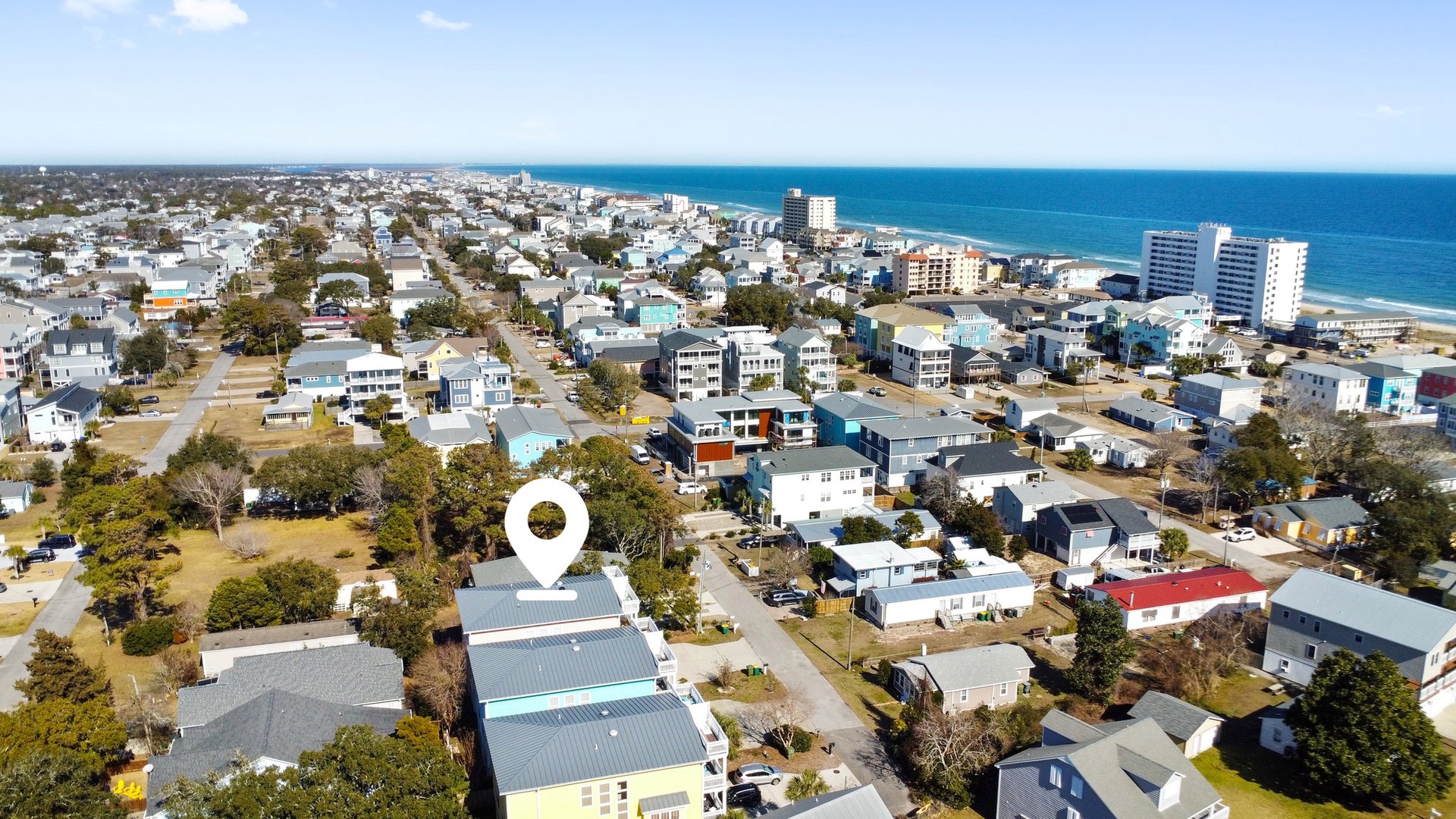 Coastal town aerial view showing residential neighborhoods with beach access and oceanfront high-rises in the distance.