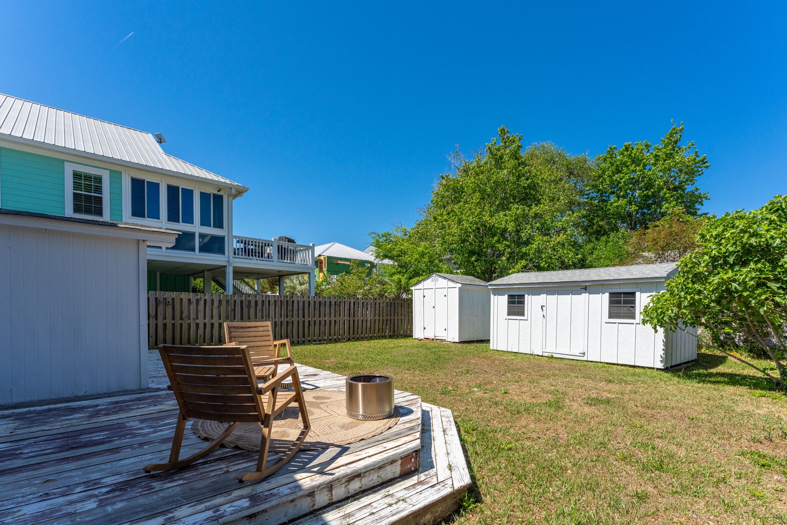 Peaceful backyard deck with wooden seating overlooking a spacious grassy area surrounded by mature trees and storage buildings.
