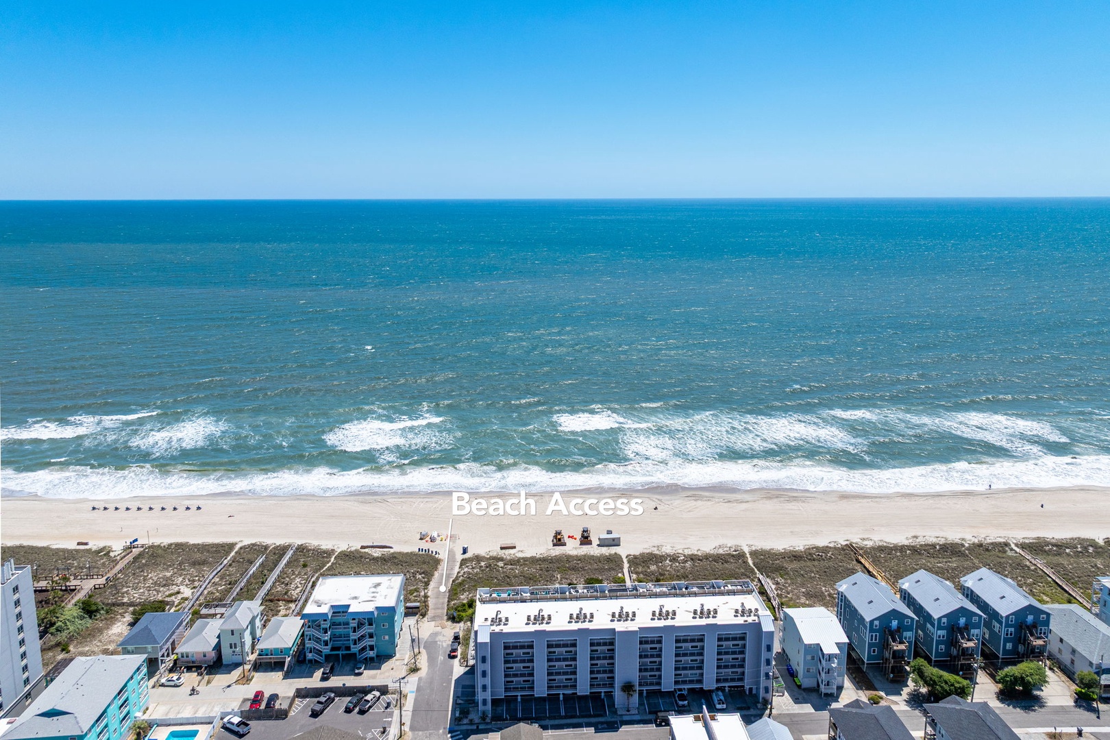 Stunning oceanfront location with direct beach access, featuring pristine sandy shores and rolling waves under brilliant blue skies.