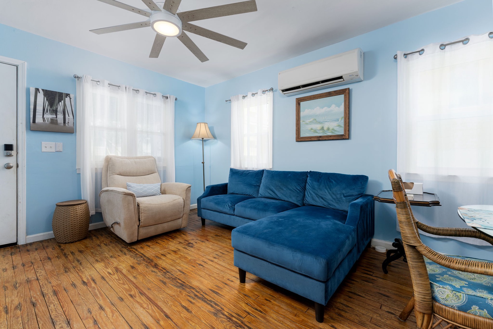 Relax in your bright living room with a plush blue sofa, cozy armchair, and hardwood floors that add warmth. A ceiling fan and air conditioning ensure comfort year-round.