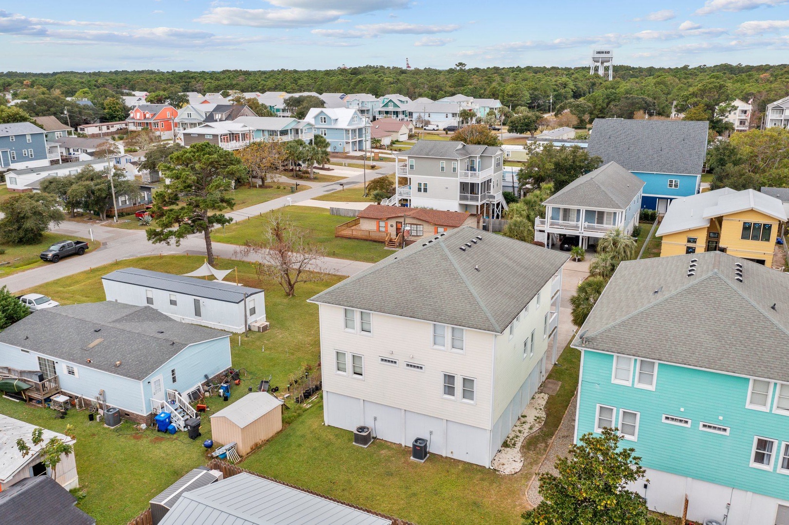 Aerial view of coastal neighborhood featuring colorful beach houses and vacation rentals surrounded by lush greenery and tree-lined streets.