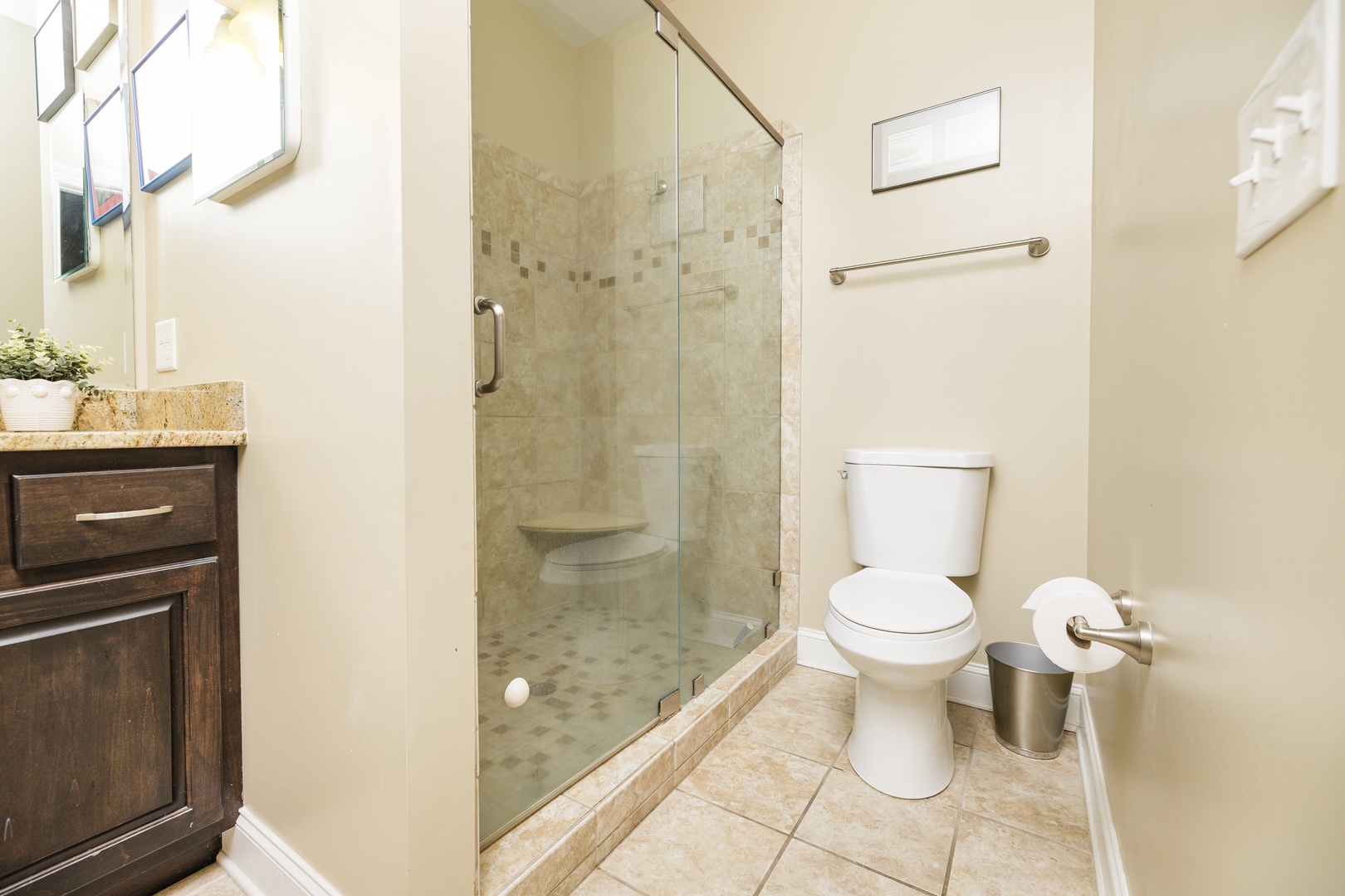 Step into your beautifully appointed bathroom featuring elegant travertine tiles, a spacious glass-enclosed shower, and refined dark wood vanity for your comfort.