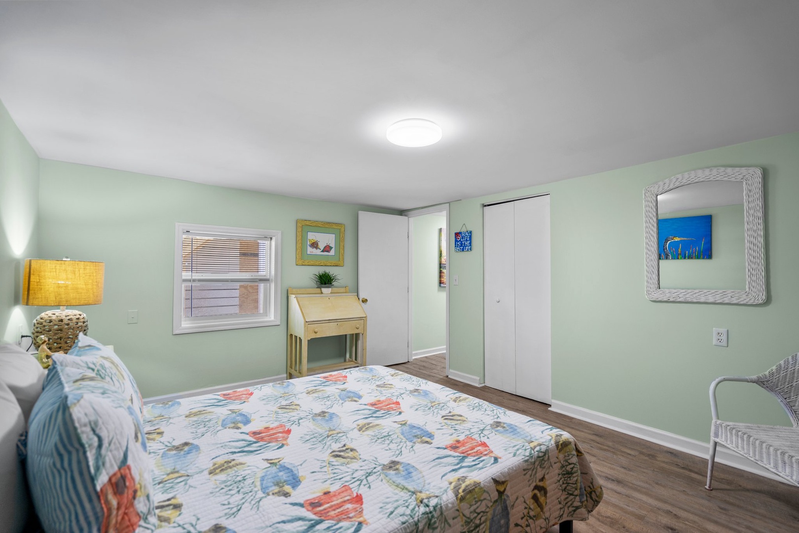 Relax in your serene mint-green bedroom with ocean-themed bedding, natural light, and coastal artwork creating a peaceful retreat.