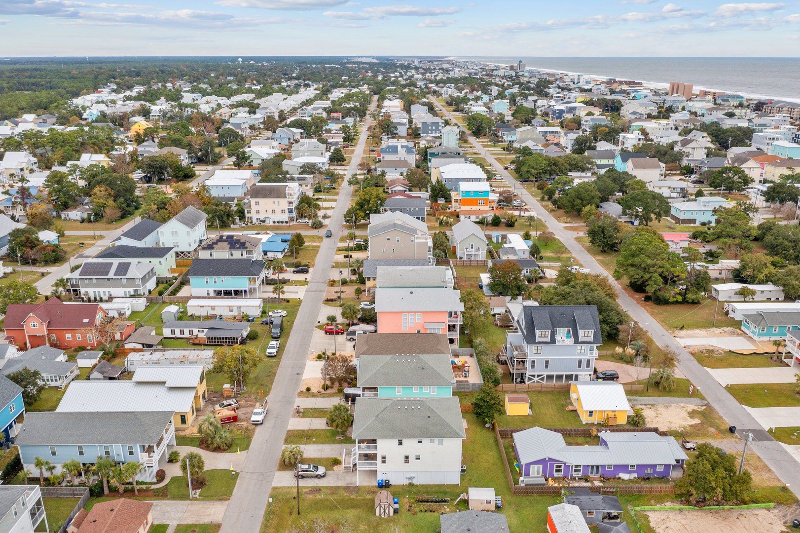 Aerial view of a charming coastal neighborhood with colorful beach houses nestled between tree-lined streets and the ocean.