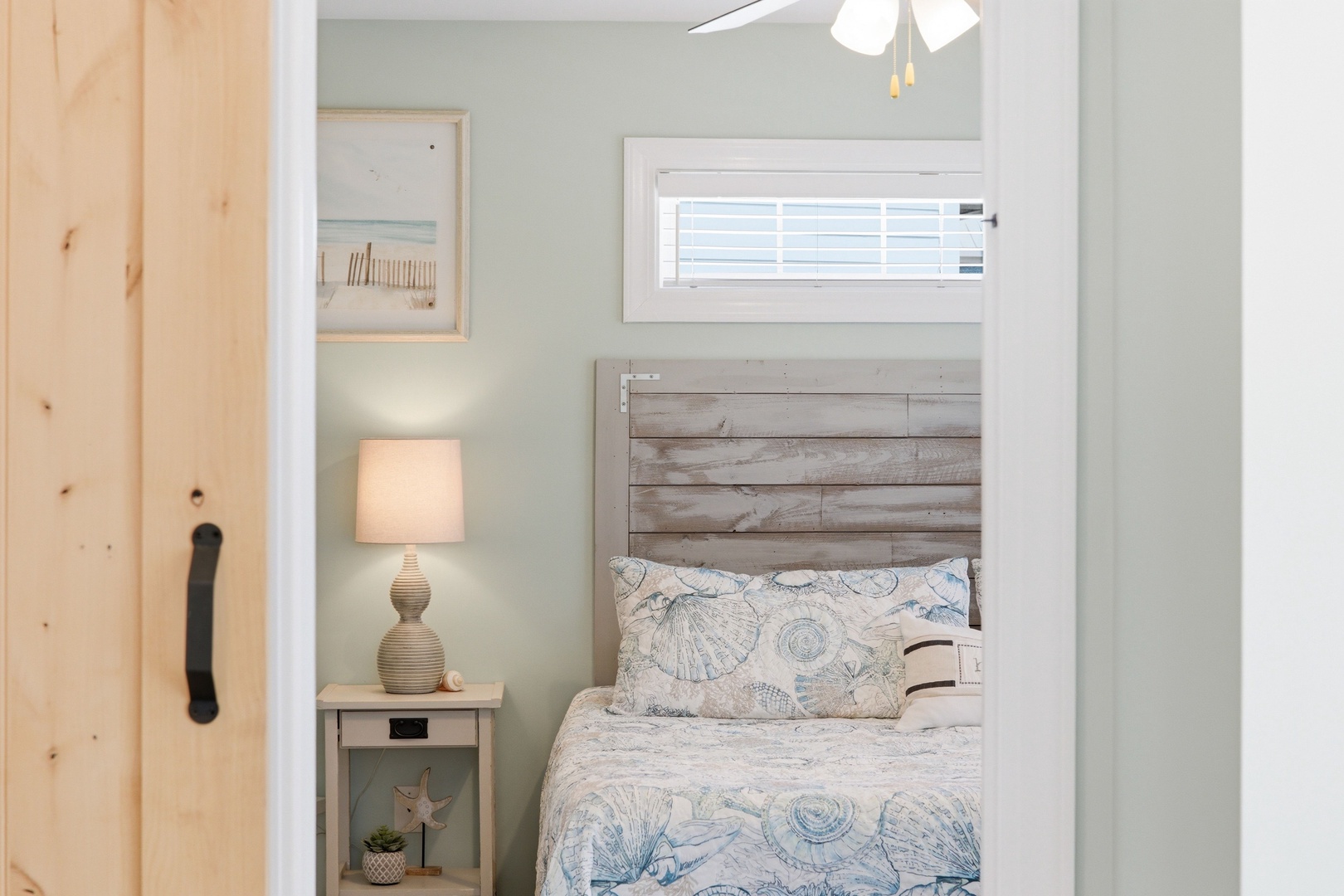 Picture yourself drifting off in this coastal-inspired bedroom, where weathered wood meets soft blue hues and gentle ceiling fan breezes. Nautical bedding and beachy artwork create your perfect seaside retreat.