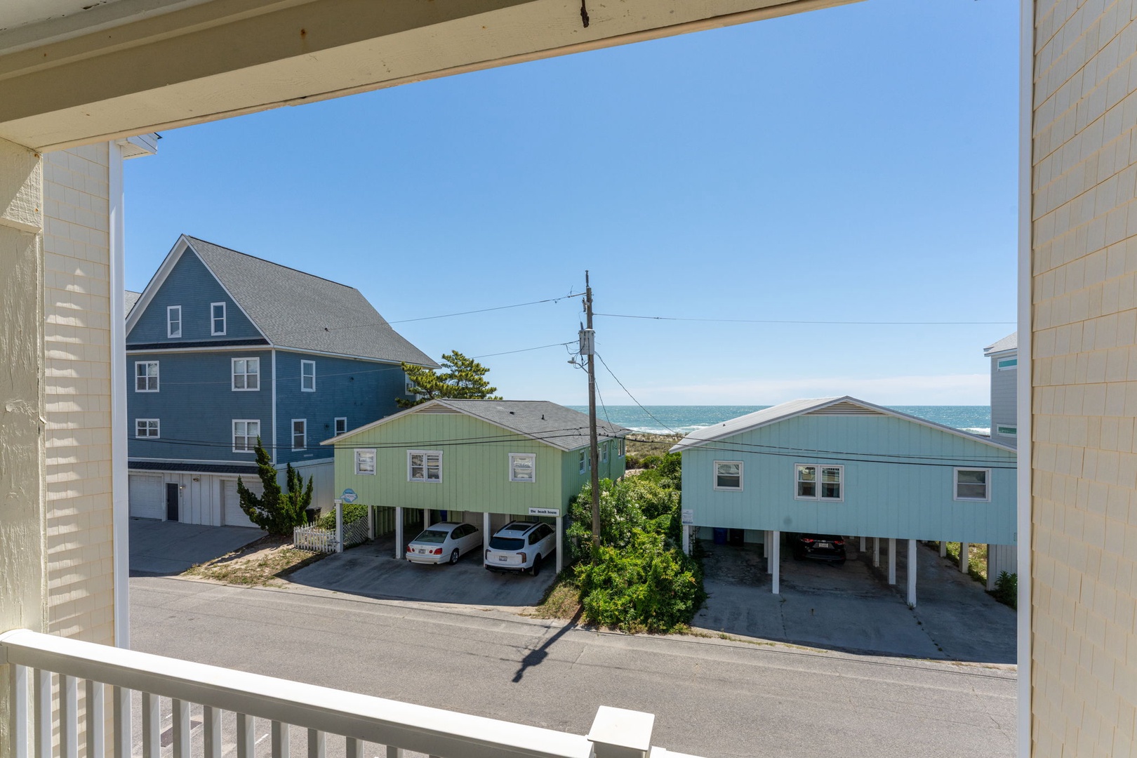 Coastal retreat framed by neighboring beach homes with glimpses of the sparkling ocean beyond—your perfect seaside escape awaits.