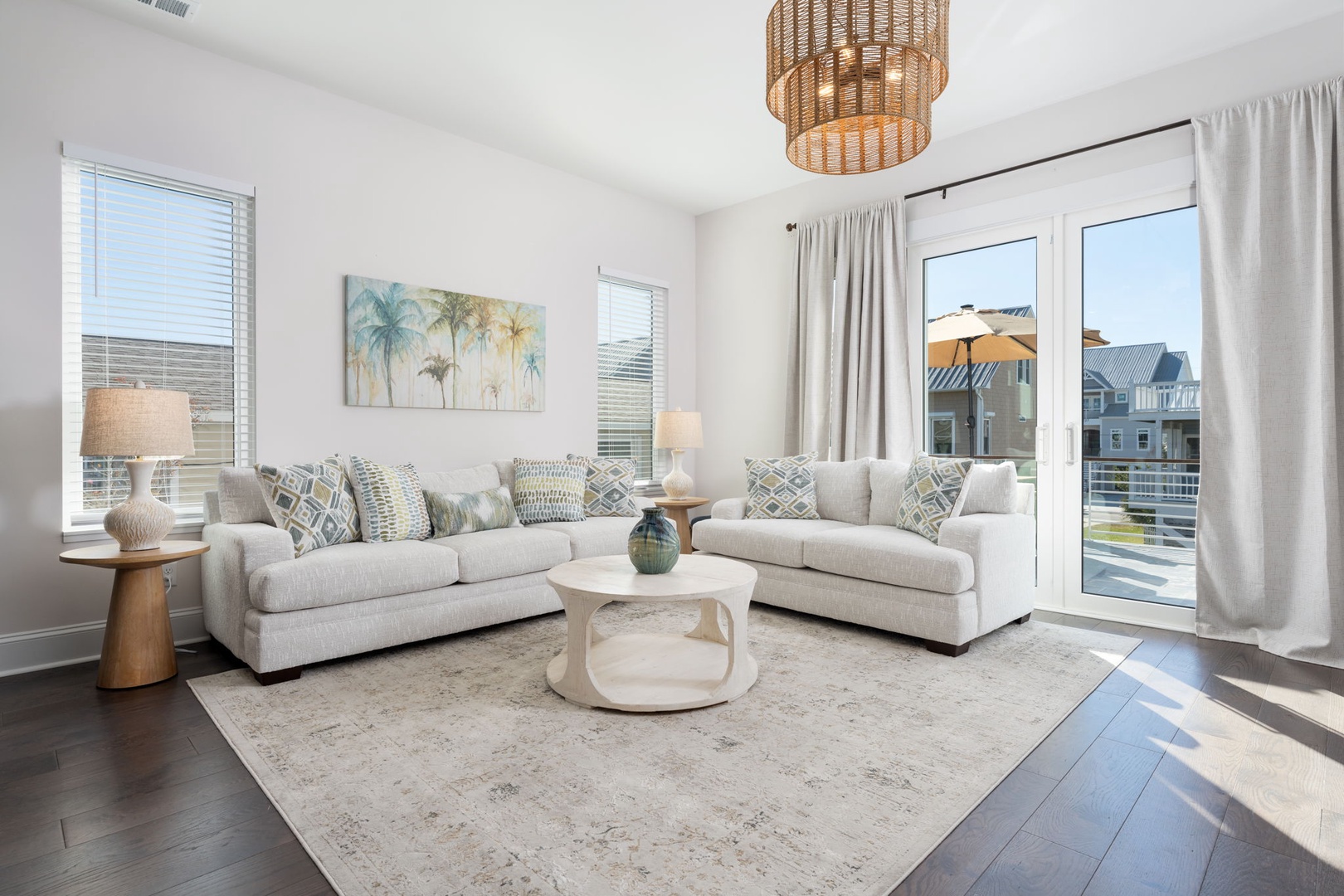 Unwind in your stylish living room with plush seating, coastal artwork, and abundant natural light streaming through large windows.