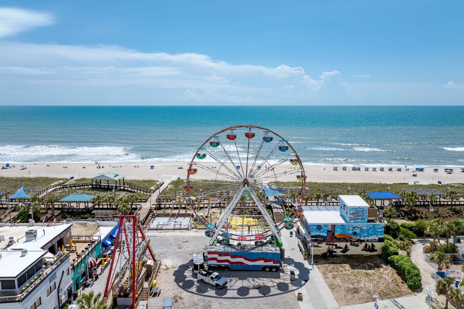 An aerial view of the beachfront area featuring a colorful Ferris wheel, amusement rides, and direct beach access—part of the lively surrounding neighborhood near the property.