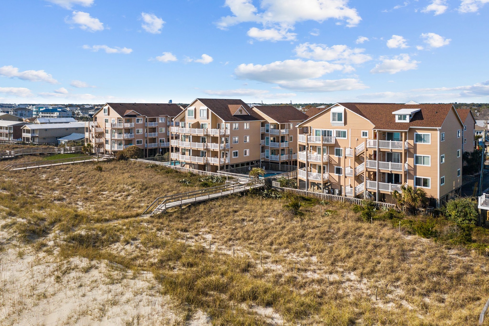 Aerial view of beachfront vacation rental buildings with natural dune landscape and wooden walkways leading to nearby coastal areas.