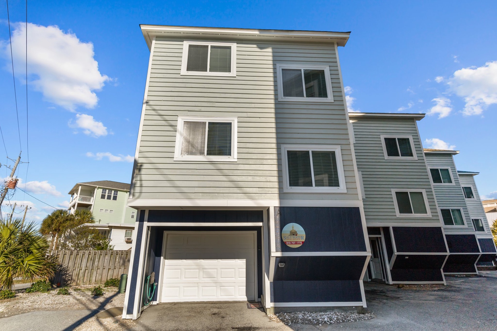 Modern beach house with private garage and coastal design, perfectly positioned among neighboring vacation rentals under bright blue skies.
