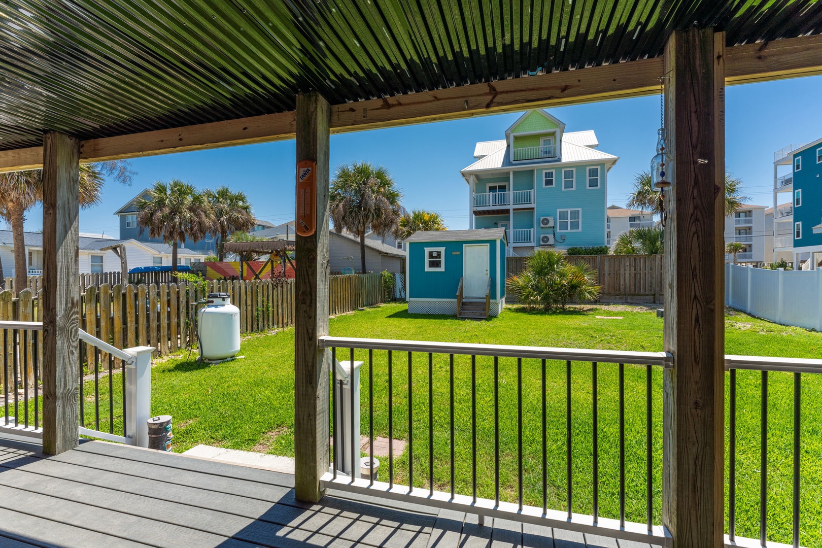 Covered patio with views of the lush lawn and neighboring coastal homes, offering a shaded spot to relax outdoors after a day at the beach.