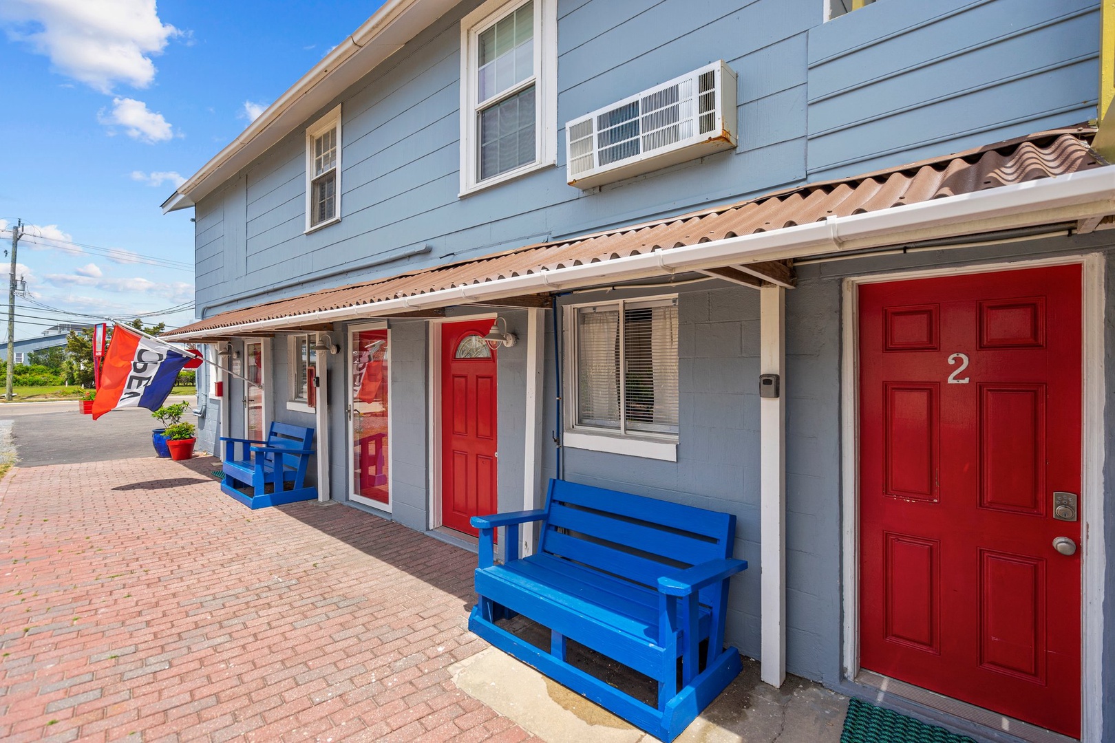 Charming beachside property with red doors and blue benches creates a welcoming coastal atmosphere for your seaside getaway.