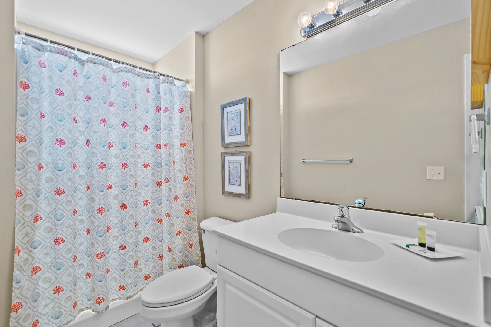 Your bright bathroom features a cheerful coral-themed shower curtain, ample vanity space, and thoughtful touches that make getting ready a pleasure.