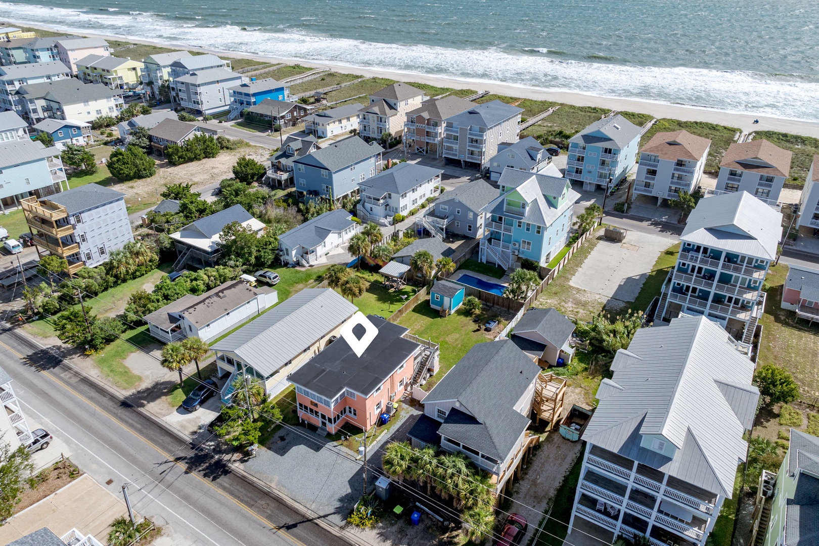 Aerial view of a charming beachfront community with colorful coastal homes, direct beach access, and pristine shoreline.
