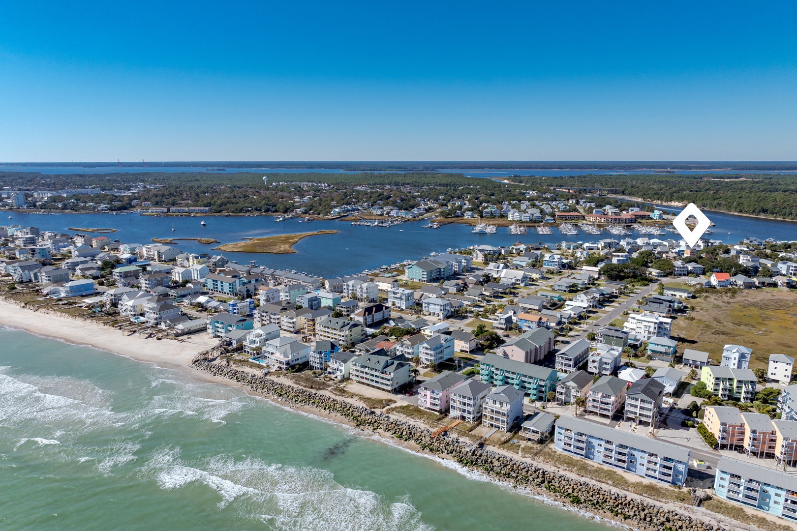 Aerial view of a charming coastal community with oceanfront properties, sandy beaches, and protected harbor waters surrounded by natural landscapes.