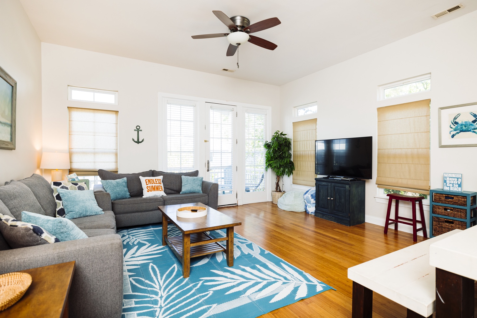 Unwind in this bright living space with coastal charm, featuring comfortable sectional seating and a ceiling fan to keep you cool.