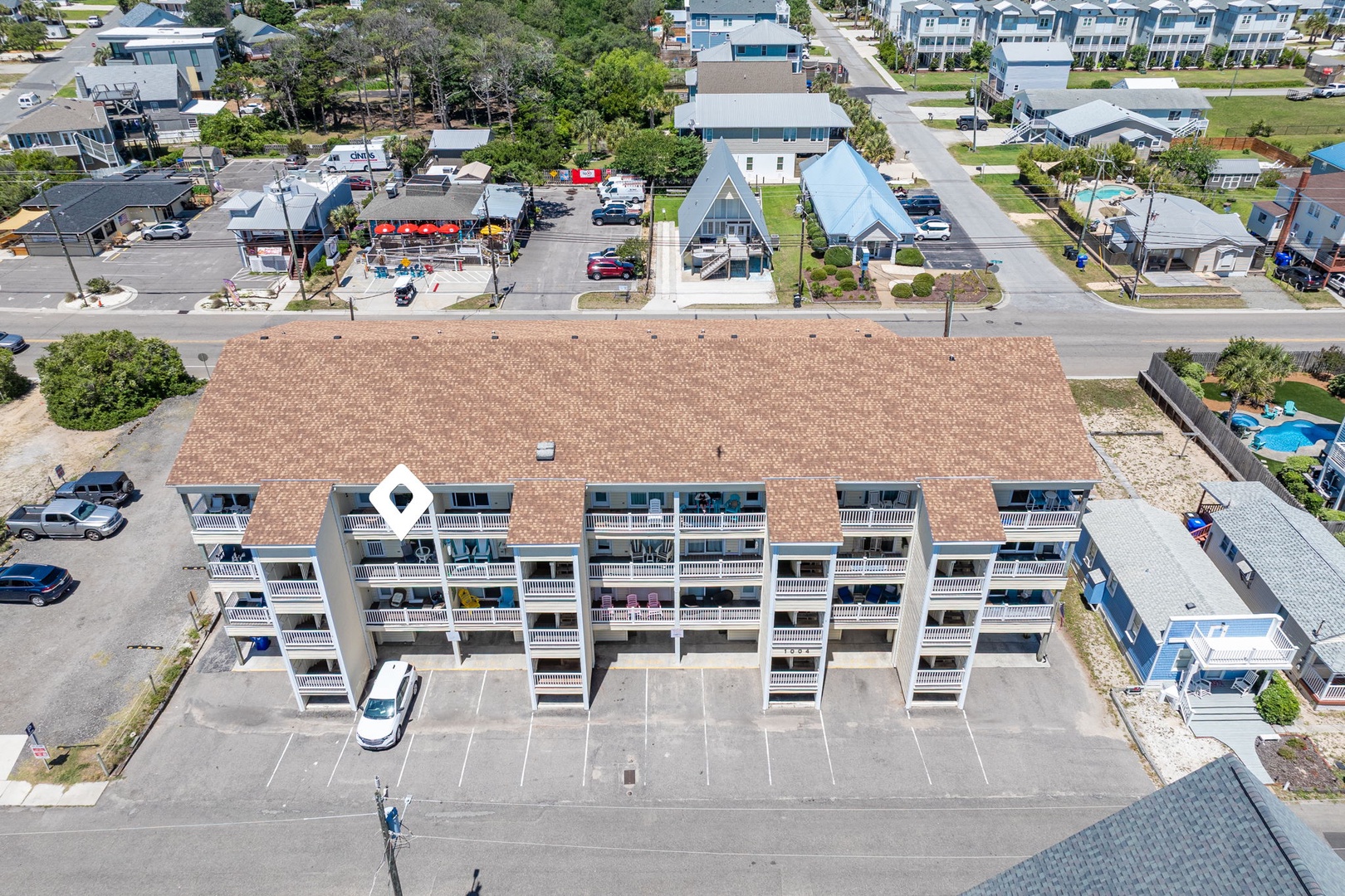 Aerial view of the property, a multi-unit coastal building with convenient parking and surrounded by a peaceful residential neighborhood near local amenities and beach access.