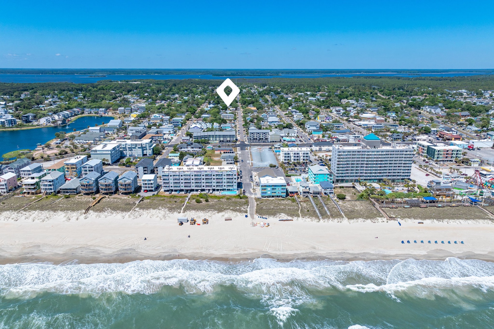 Aerial view of beachfront community with sandy shore and ocean waves, featuring mixed residential and commercial development.