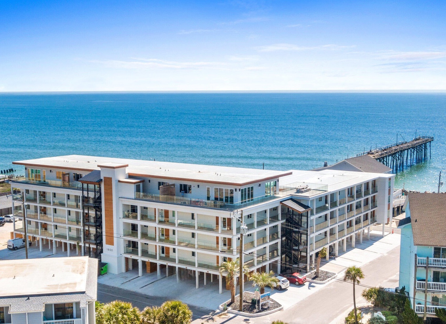 Modern beachfront property sits directly on pristine coastal sands with fishing pier and endless ocean views stretching to the horizon.