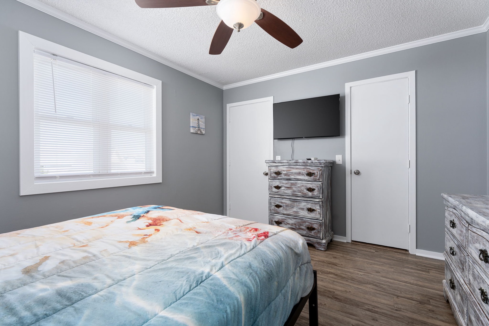 Unwind in your peaceful bedroom with soft gray walls, a cozy bed, and a gentle ceiling fan overhead. Natural light fills the space, while your entertainment and storage needs are met effortlessly.