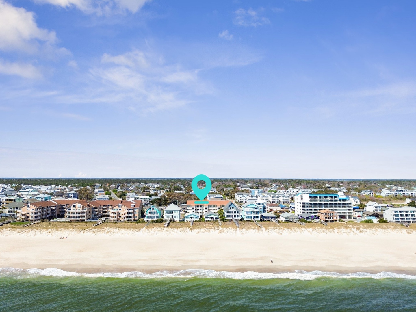 Aerial view of beachfront vacation rentals nestled between pristine sandy beach and residential neighborhood.