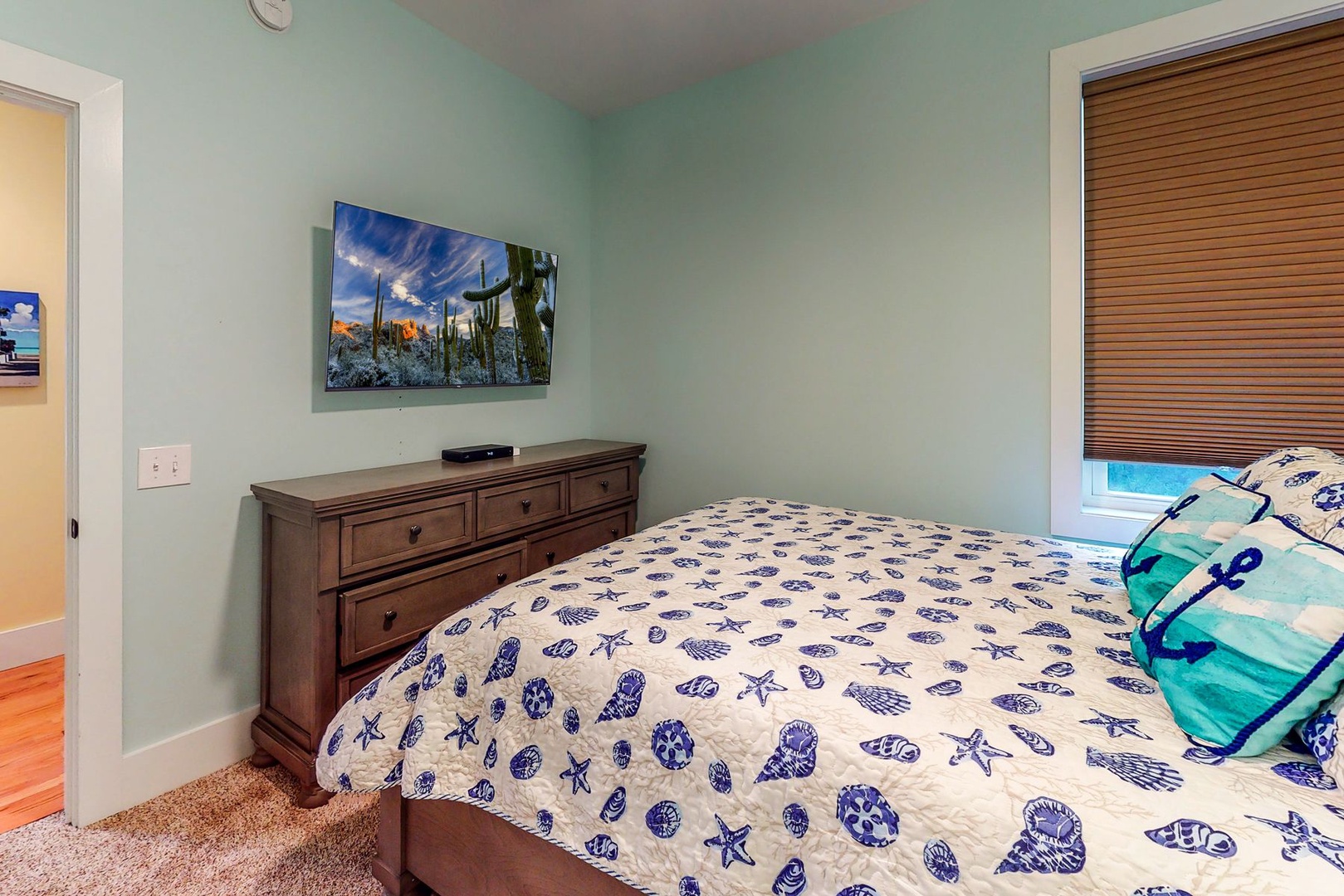Sink into your cozy bedroom with ocean-themed bedding and desert art, where wooden blinds filter gentle light for perfect rest.