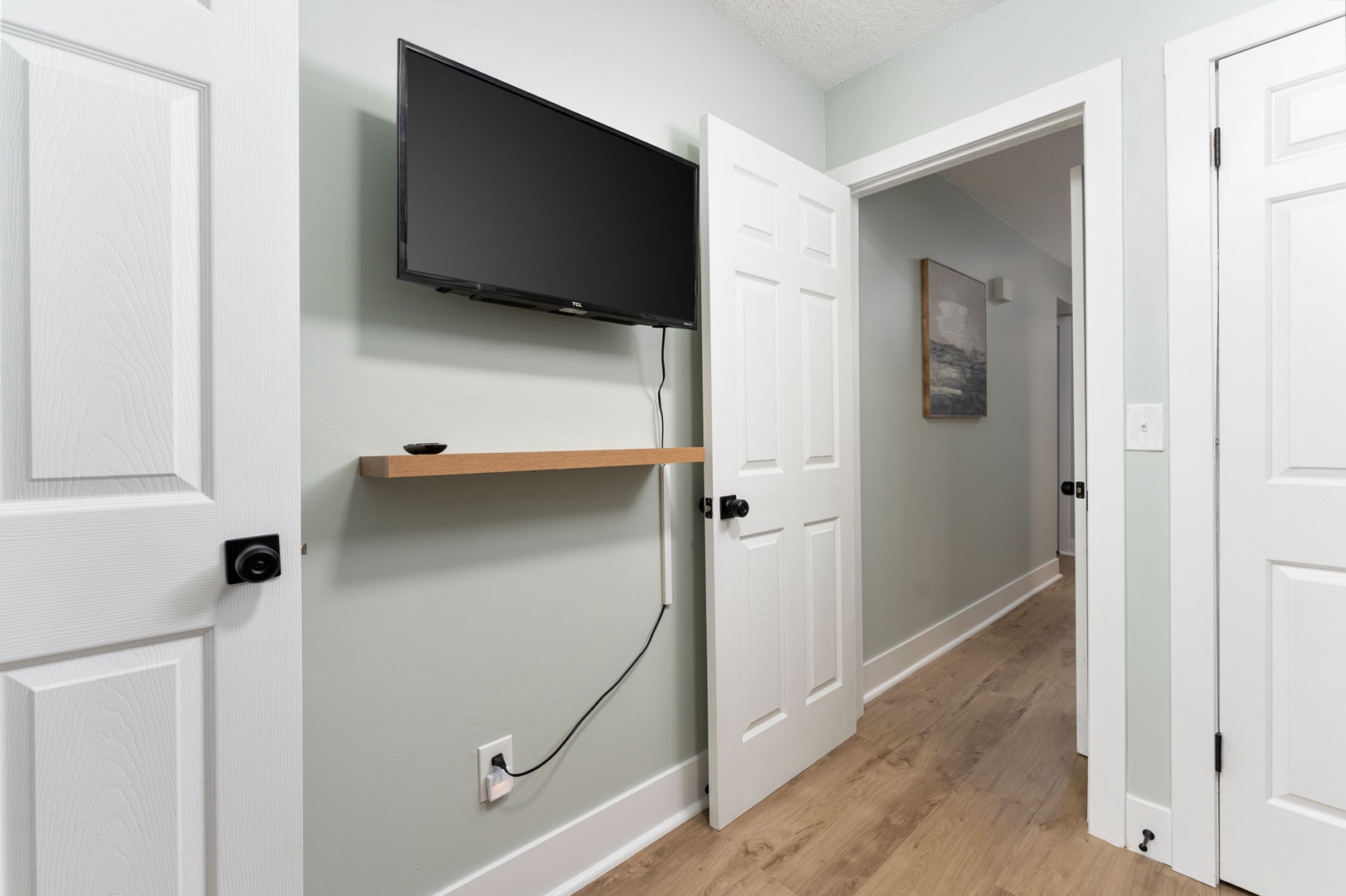 Step into your private hallway, where a wall-mounted TV and clean modern finishes set the tone for comfort. Warm wood floors and soft gray walls create a calm, welcoming retreat.