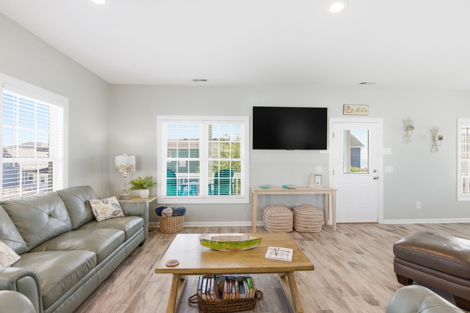 Relax in your airy living room with plush leather seating, a large flat-screen TV, and natural light pouring through elegant plantation shutters. Step outside to glimpse the pool just beyond your door.
