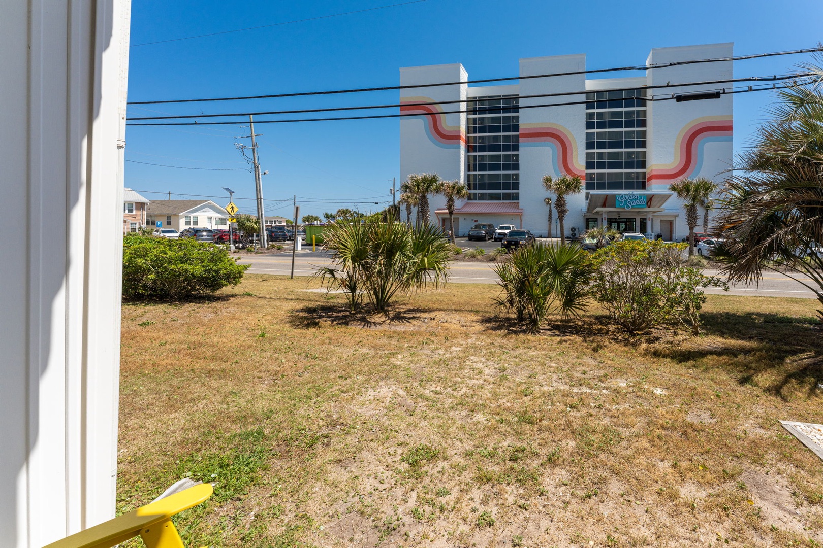 View across the street showcases the colorful beachside neighborhood with tropical palm landscaping and local businesses nearby.