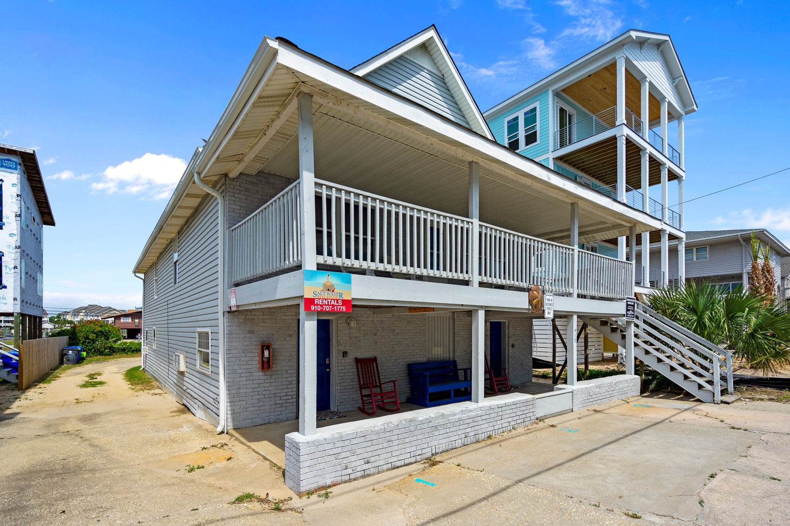 Spacious beach house with covered porches and stairs leading to upper-level balcony, situated in coastal neighborhood.