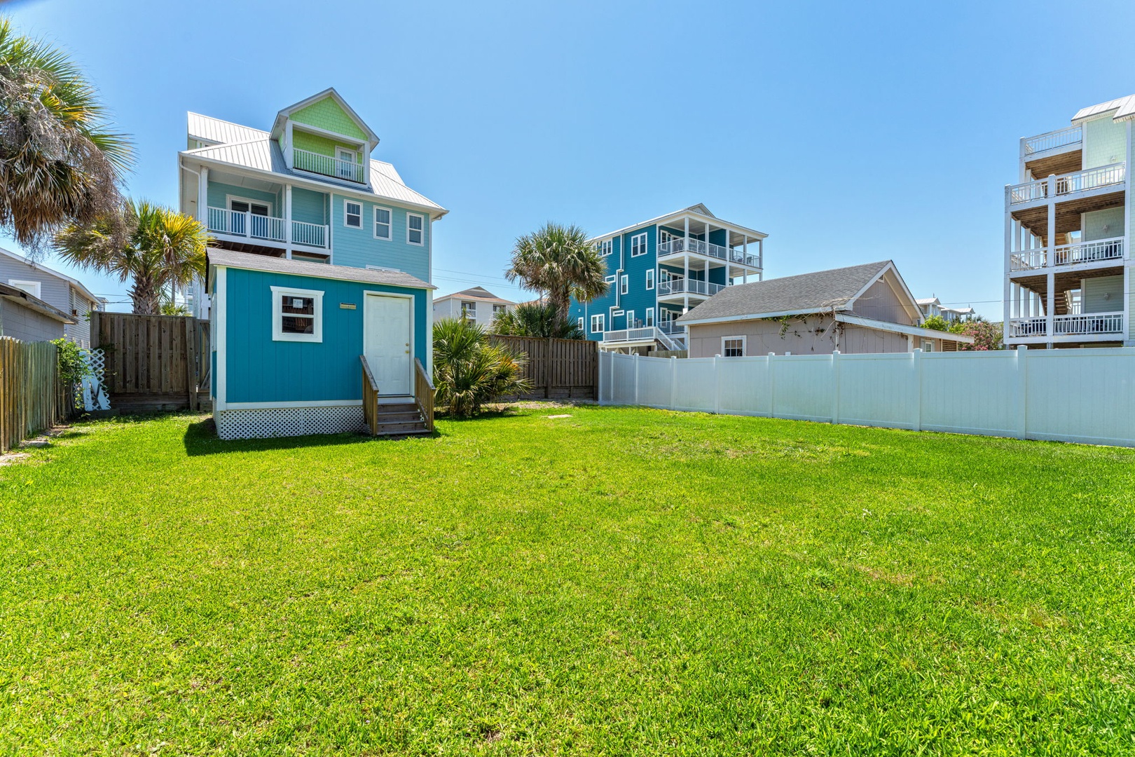 This charming coastal property features a vibrant turquoise exterior with white accents, spacious lawn, and tropical palm trees, located in a peaceful beach neighborhood with ocean views.