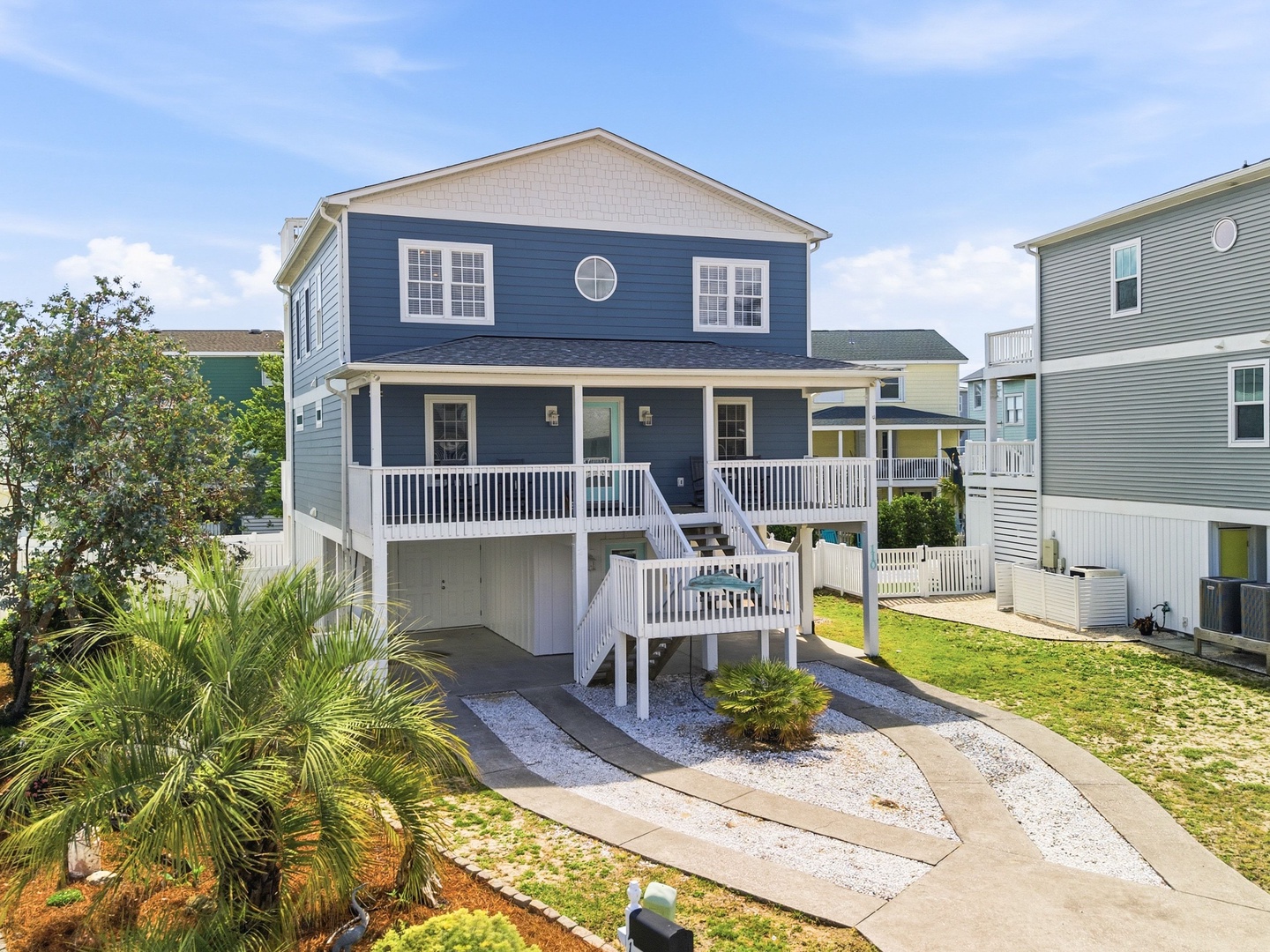 Elevated coastal cottage with wraparound porch, landscaped walkways, and beach-inspired styling nestled in a friendly residential neighborhood.