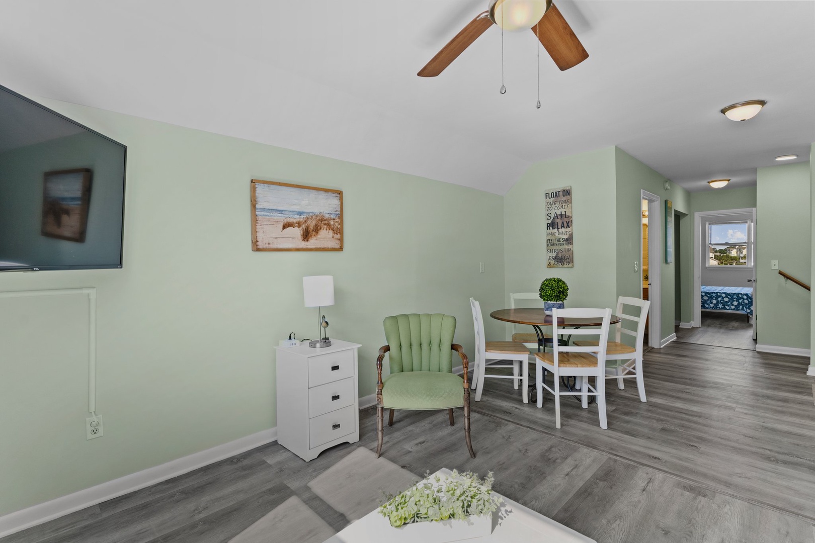 Relax in your bright, coastal-themed living space where soft green walls and beach artwork create a serene atmosphere for unwinding.