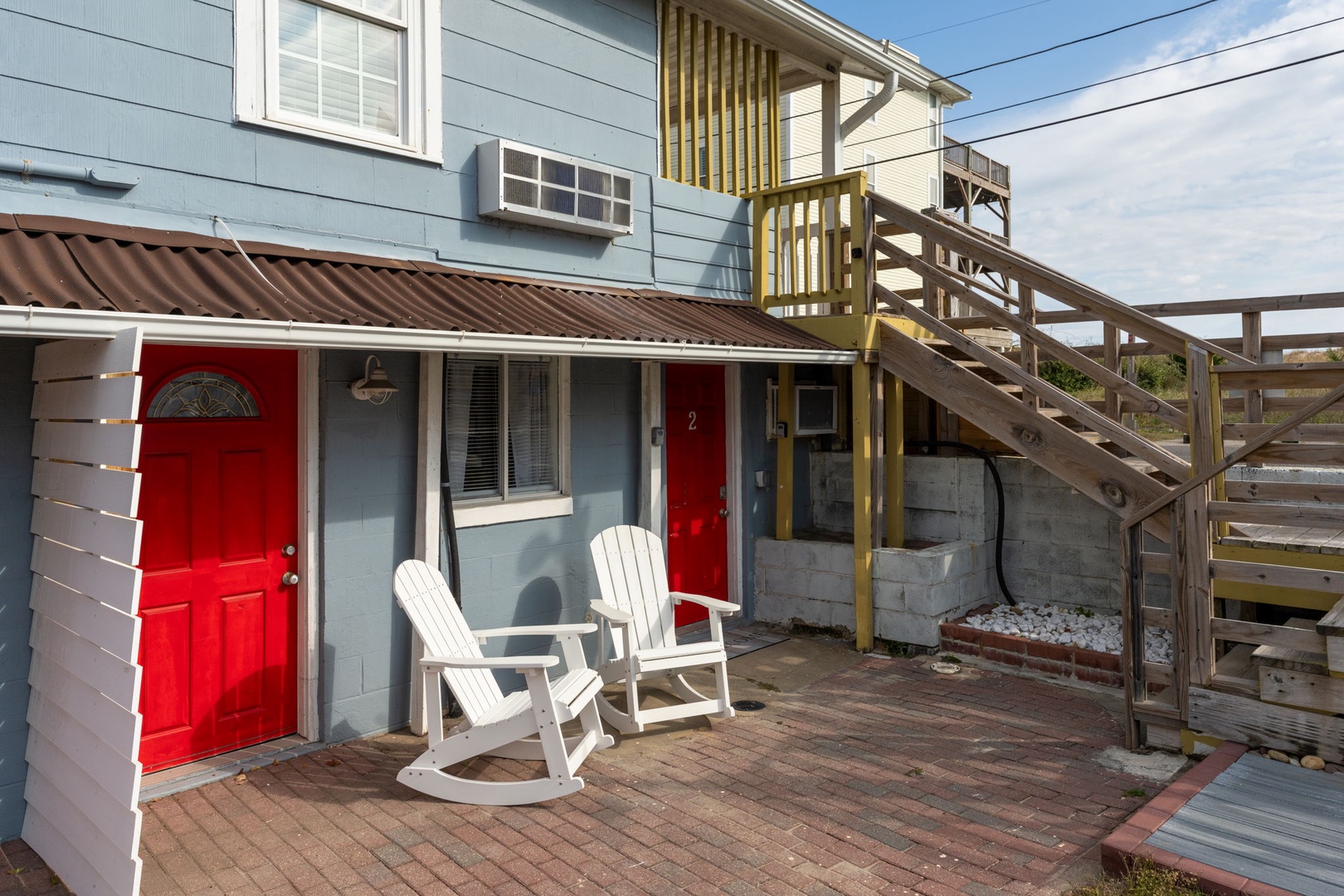 Charming coastal cottage with bright red door and cozy white rockers where you can unwind after beach adventures.