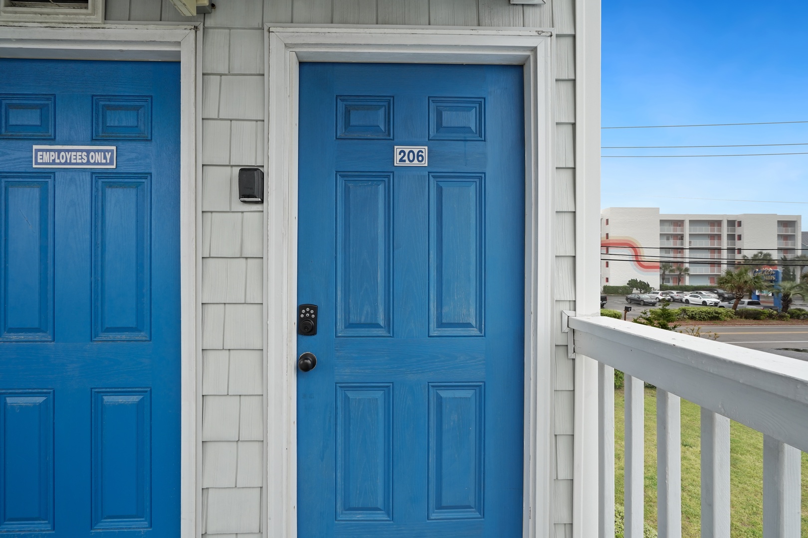Bright blue door welcomes you to room 206, where your coastal getaway begins with clear skies and nearby amenities.