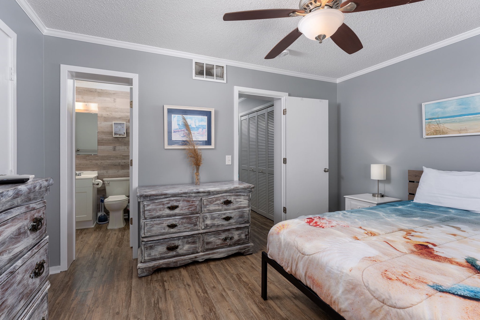 Relax in your cozy bedroom with soft gray walls, a comfortable bed, and calming beach artwork. Enjoy the ceiling fan and an ensuite bathroom just steps away.
