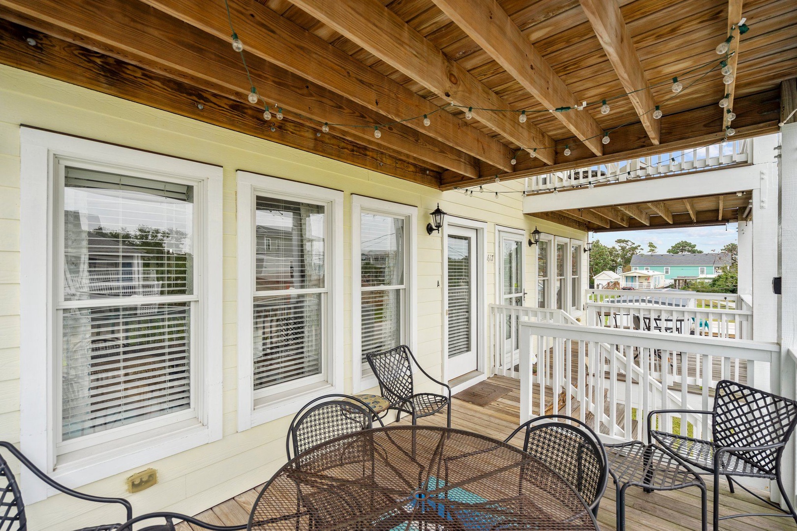 Step onto your private covered balcony where coastal breezes meet comfortable seating under charming string lights and exposed wooden beams overhead.