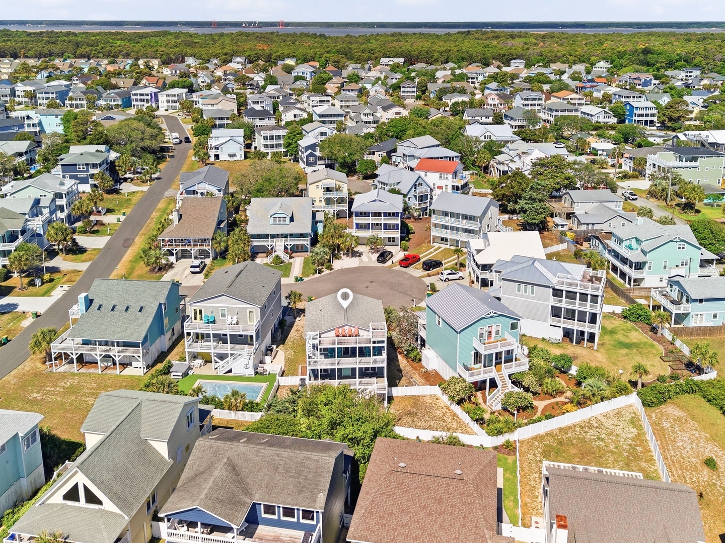 Aerial view of a charming coastal neighborhood with the rental property nestled among beach homes, surrounded by greenery and close to the waterfront.
