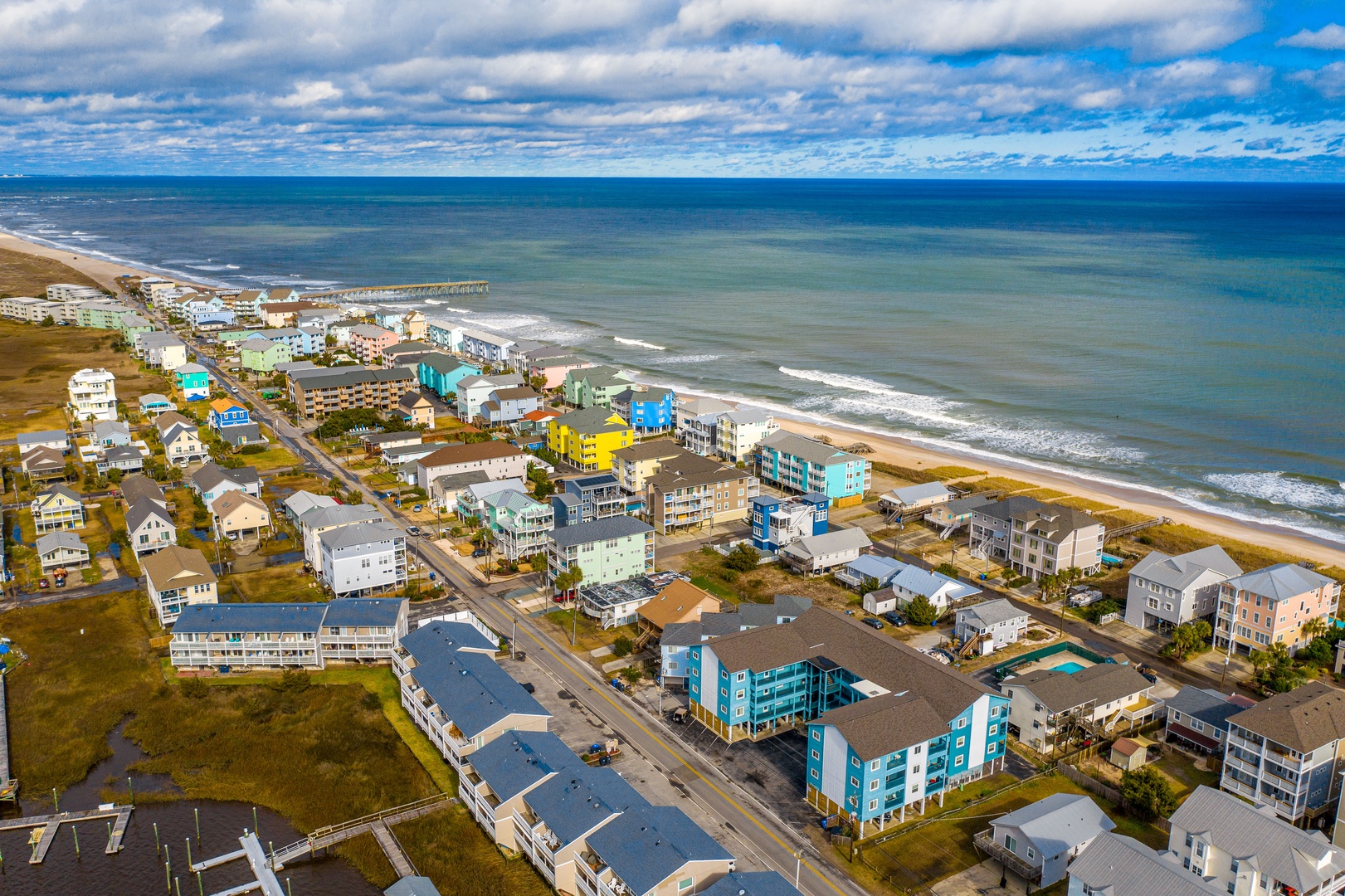 Aerial view of a vibrant coastal community with colorful beachfront homes and pristine sandy shores stretching along the Atlantic Ocean.