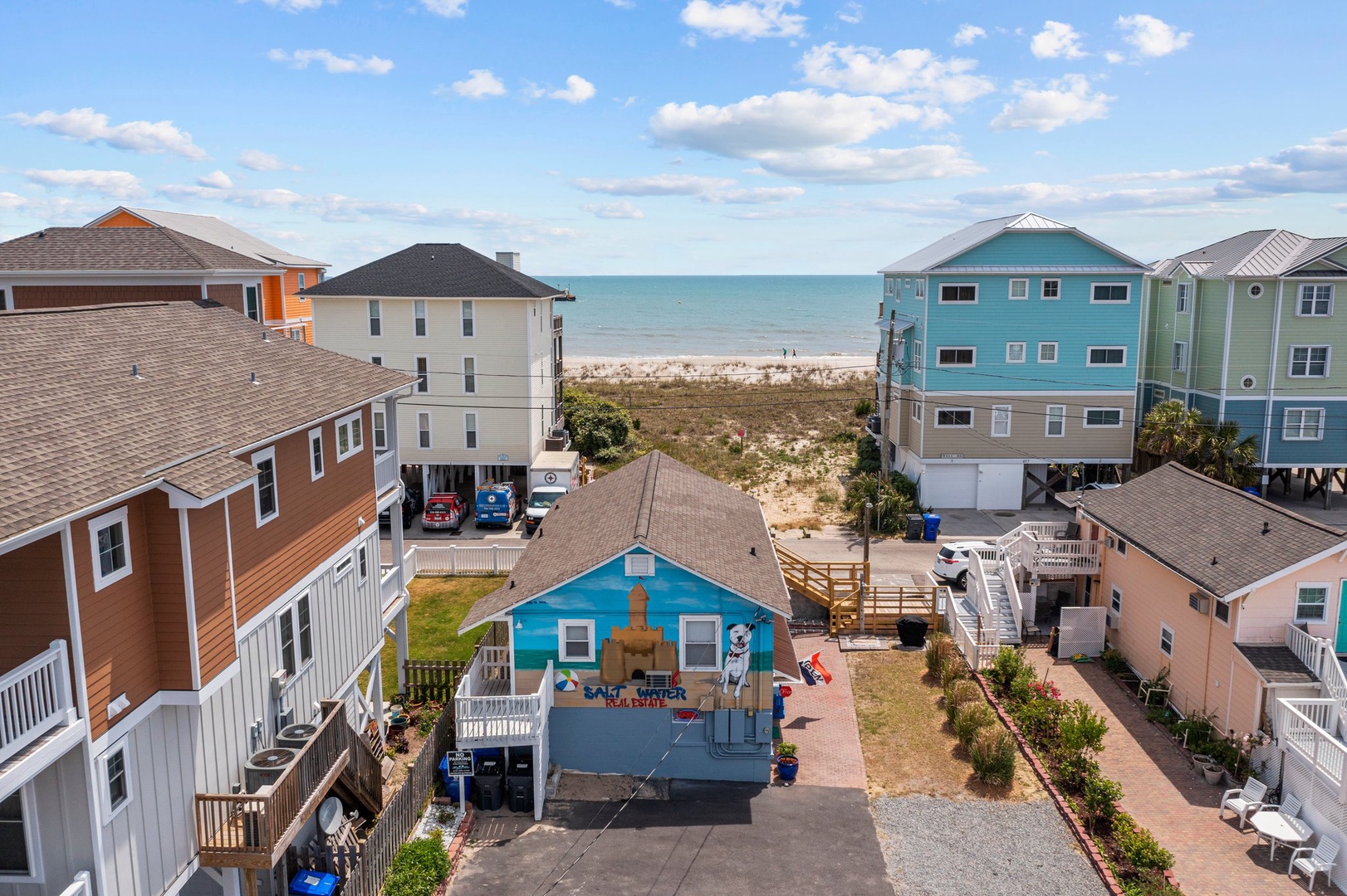 Aerial view of colorful beach houses nestled between residential streets and pristine oceanfront with sandy shores.