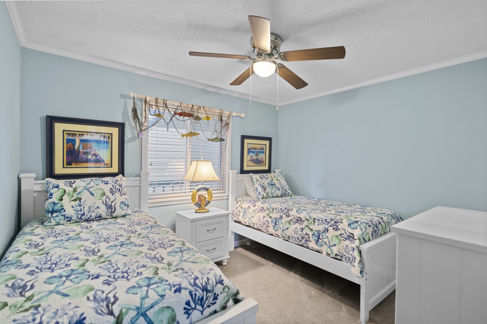 Your coastal-themed twin bedroom features crisp white beds with ocean-inspired linens, perfect for peaceful nights under the gentle ceiling fan.