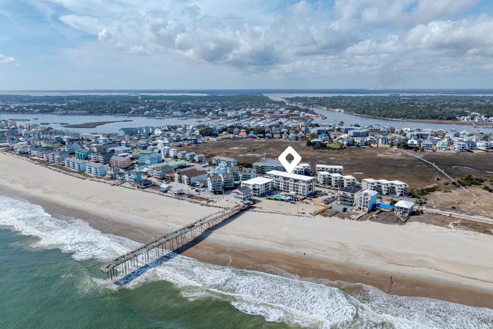 Aerial view of beachfront property nestled between pristine coastline and charming coastal community with fishing pier and waterways.
