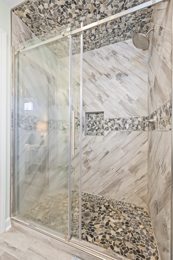 Step into your luxurious walk-in shower with stunning pebble accents and wood-look tile. The spacious design and rainfall showerhead invite pure relaxation after exploring the area.